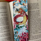 Handgemachtes Lesezeichen mit Drachenmotiv und roter Quaste in einem Buch.